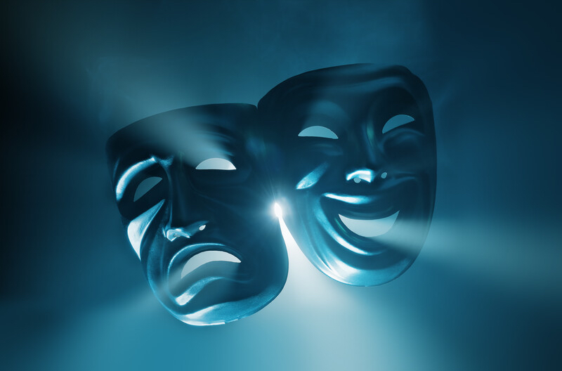 Light behind and shining through two theatre masks - one happy, one sad